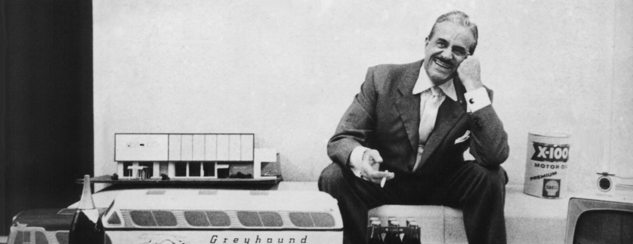 Raymond Loewy sitting with cigarette in hand and Greyhound bus model on table